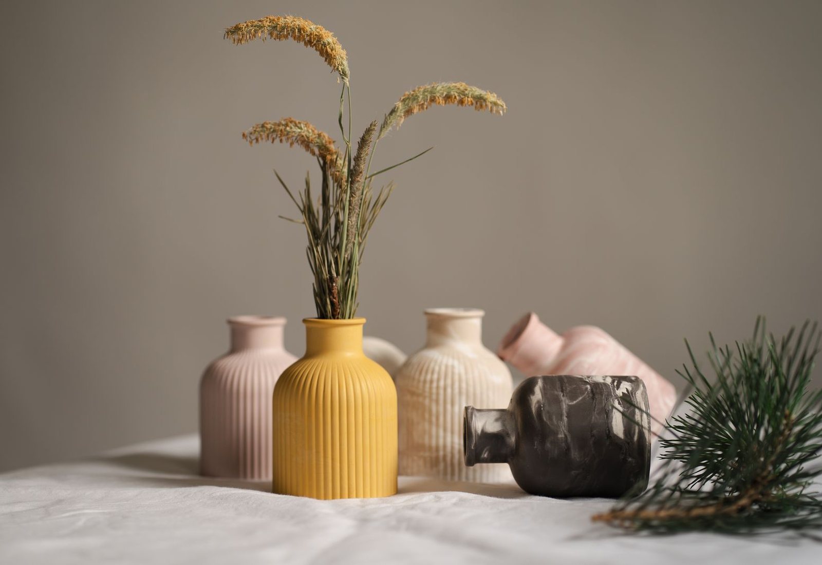 Vasos de cerâmica em tons de amarelo, rosa e cinza sobre uma mesa clara